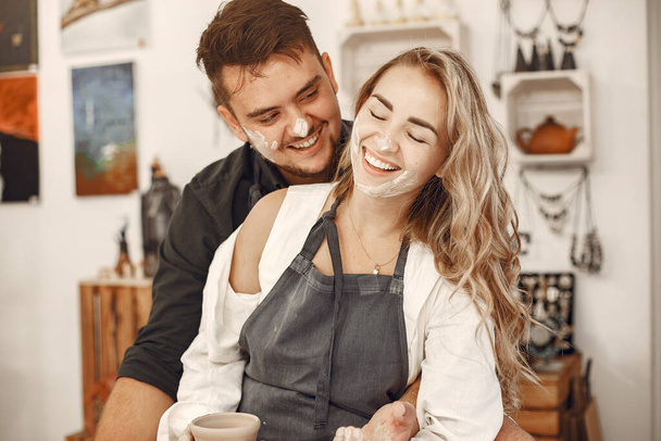 Mutual creative work. Young beautiful couple in casual clothes and aprons. People creating a bowl on a pottery wheel in a clay studio. - Foto, imagen