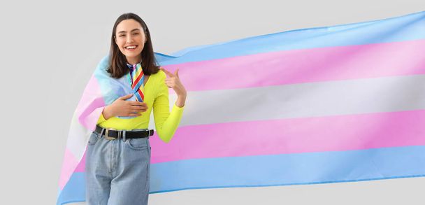 Молода жінка з трансгендерним прапором на світлому фоні
 - Фото, зображення