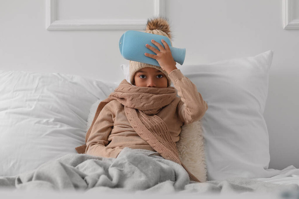 Ill African-American boy warming his head with hot water bottle in bedroom - Foto, Imagem