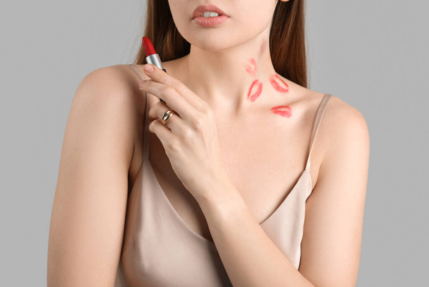 Mujer joven con marcas de lápiz labial y mordedura de amor en el cuello contra fondo gris, primer plano - Foto, Imagen