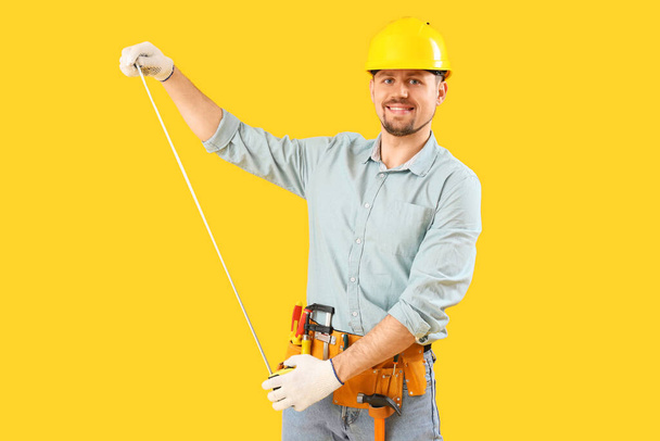 Male carpenter with measure tape on yellow background - Фото, зображення