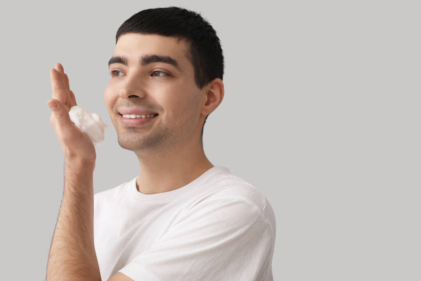Hombre joven aplicando espuma de afeitar en la cara contra el fondo claro - Foto, Imagen