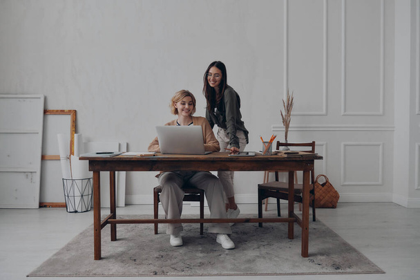 Two happy young businesswomen using laptop while working together at the creative office - Фото, зображення
