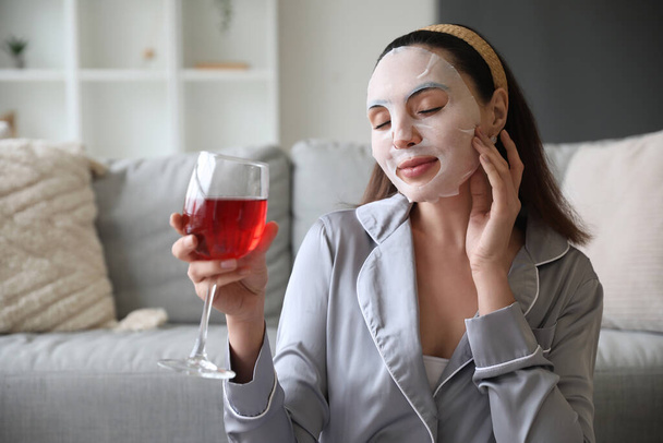 Молодая женщина в маске и бокале вина дома - Фото, изображение