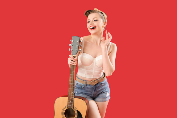 Молодая пинап-женщина с гитарой на красном фоне - Фото, изображение