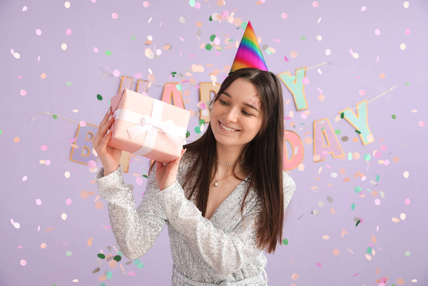 Glückliche junge Frau mit Geschenk feiert Geburtstag auf fliederfarbenem Hintergrund - Foto, Bild