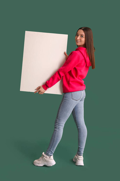 Young woman in hoodie with big blank poster on green background - Foto, immagini