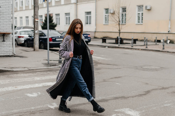 Μια γυναίκα διασχίζει το δρόμο με παλτό και τζιν. - Φωτογραφία, εικόνα