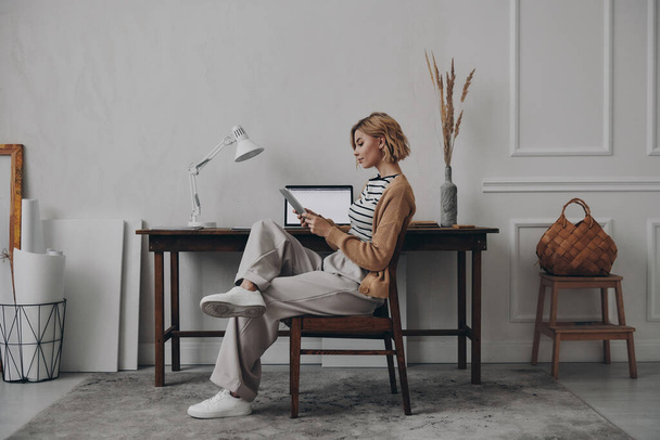 Αυτοπεποίθηση νεαρή γυναίκα χρησιμοποιώντας ψηφιακή ταμπλέτα ενώ κάθεται στο δημιουργικό χώρο εργασίας της - Φωτογραφία, εικόνα