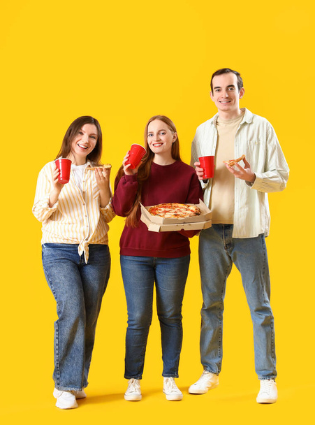 Happy friends with tasty pizza and drinks on yellow background - Photo, image