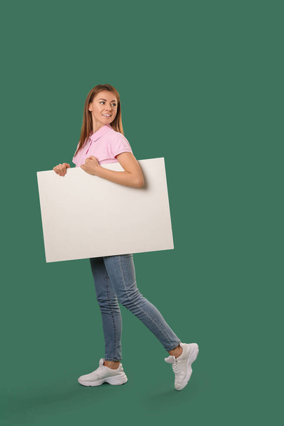 Beautiful woman with big blank poster on green background - Photo, image
