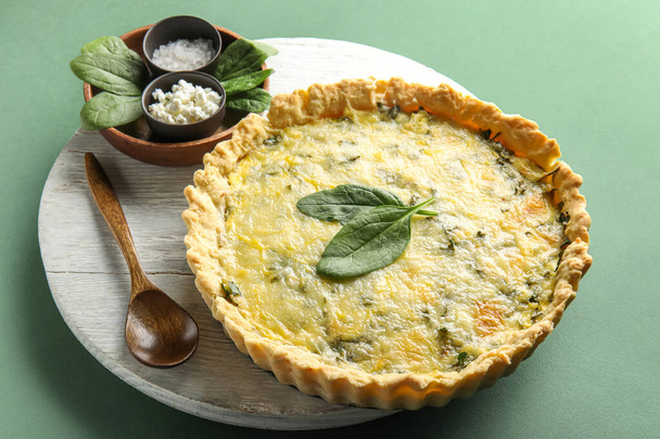 Board with delicious quiche, cottage, salt and spinach leaves on green background - Photo, Image