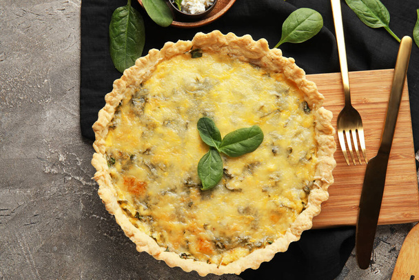Brett mit köstlicher Quiche, Spinatblättern und Feta-Käse auf grauem Grunge-Hintergrund - Foto, Bild