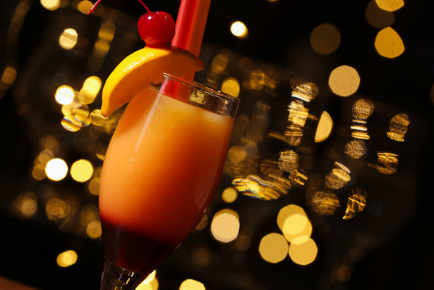 Glass of tasty Tequila Sunrise against blurred lights, closeup - Photo, Image