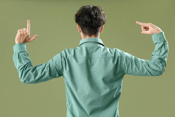 Junger Mann zeigt Verlierer-Geste auf grünem Hintergrund, Rückansicht - Foto, Bild