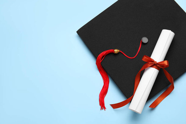 Diploma con cinta roja y sombrero de graduación sobre fondo azul - Foto, imagen