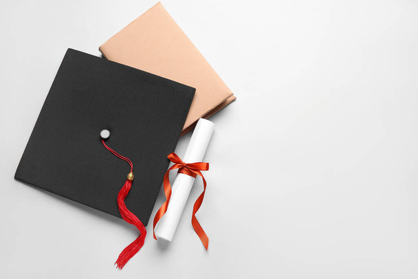 Diploma met rood lint, afstudeerhoed en boek over witte achtergrond - Foto, afbeelding
