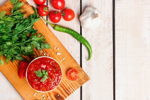 Board with bowl of delicious salsa sauce and ingredients on white wooden table - Photo, Image