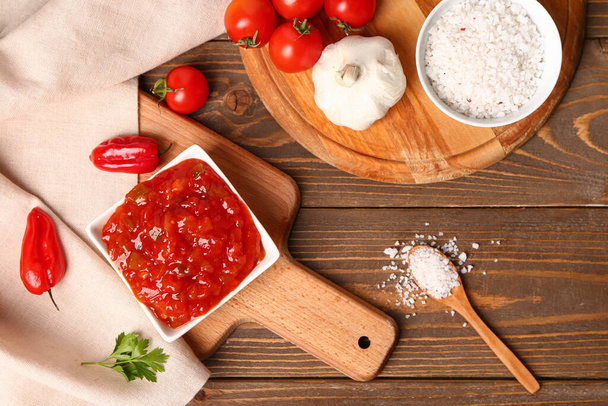 Koostumus kulhoon herkullista salsa kastiketta ja ainesosia ruskea puinen pöytä - Valokuva, kuva