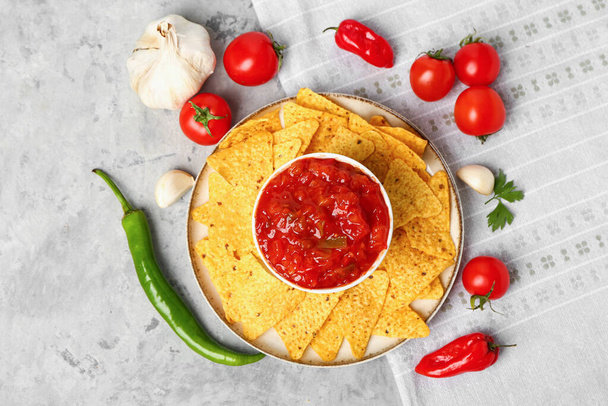 Samenstelling met kom heerlijke salsasaus, nacho 's en ingrediënten op grijze grunge achtergrond - Foto, afbeelding