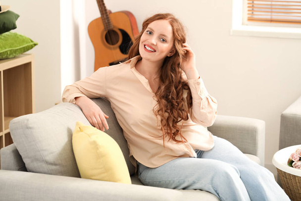 Evdeki kanepede oturan güzel kızıl saçlı kadın. - Fotoğraf, Görsel