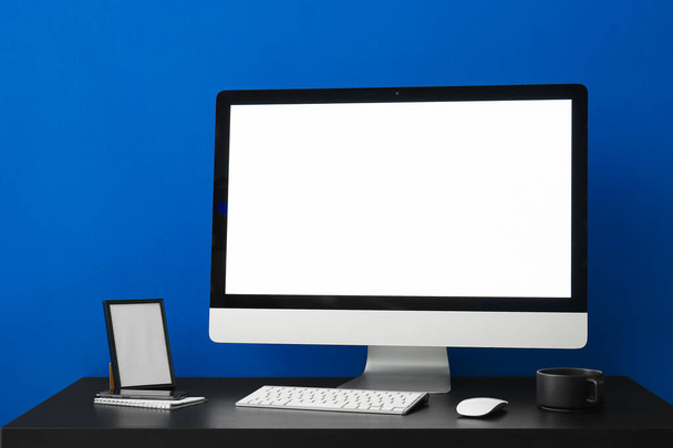 Lugar de trabajo con ordenador, marco y taza cerca de la pared azul - Foto, imagen