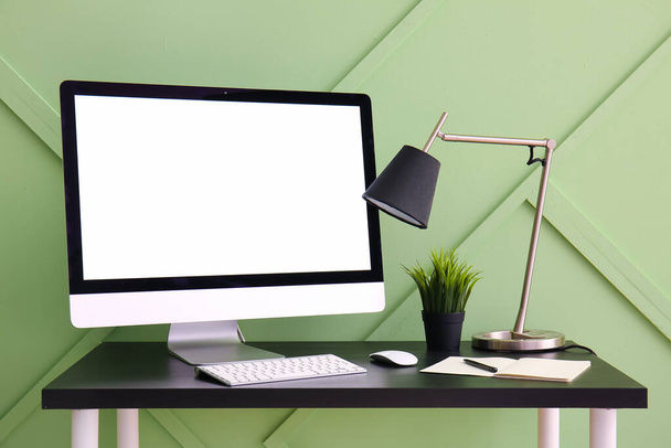 Lugar de trabajo con ordenador y lámpara cerca de la pared verde - Foto, imagen