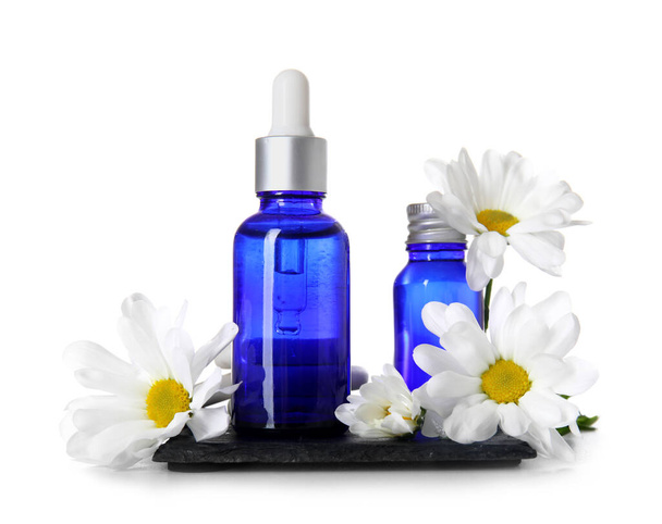 Composizione con bottiglie di olio per cuticole e fiori di camomilla su fondo bianco - Foto, immagini
