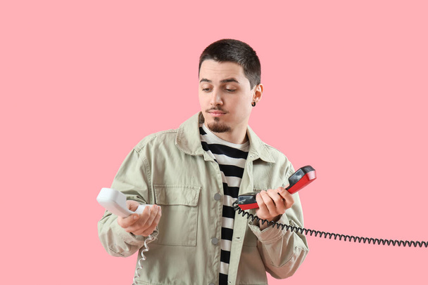 Komea nuori mies, jolla on kaksi puhelimen vastaanotinta vaaleanpunaisella taustalla - Valokuva, kuva