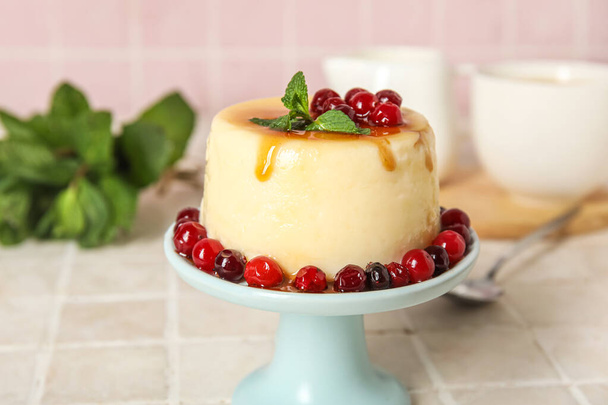 Dessert stand with delicious pudding, mint and cranberries covered by caramel syrup on tile background - Zdjęcie, obraz