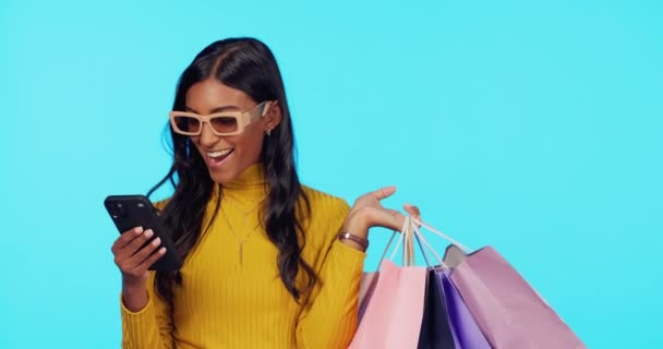 Happy woman, phone and shopping bags in studio for purchase, sale or discount against a blue background. Portrait of female shopper smile with smartphone for fashion, buying or social media on mockup. - Footage, Video