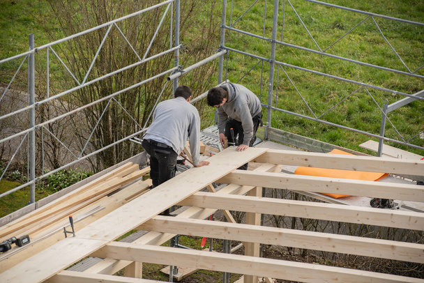 Δύο νεαροί ξυλουργοί χτίζουν ένα υπόστεγο. Μαθητευόμενος μαθαίνει από εκπαιδευτής. - Φωτογραφία, εικόνα