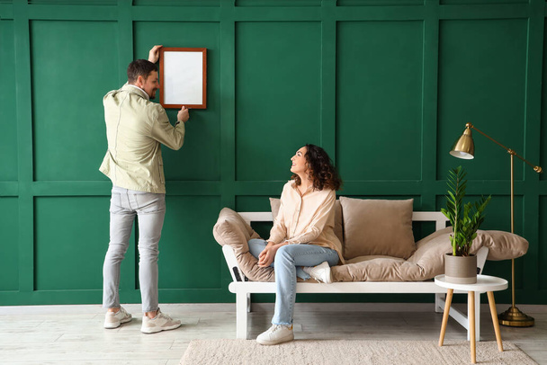 Casal jovem pendurado quadro em branco na parede verde em casa - Foto, Imagem