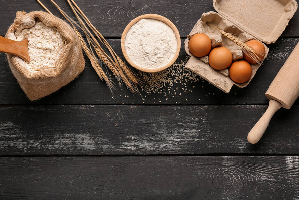 Skład z mąki, kłosów pszenicy, jaj i wałka na czarnym drewnianym stole - Zdjęcie, obraz