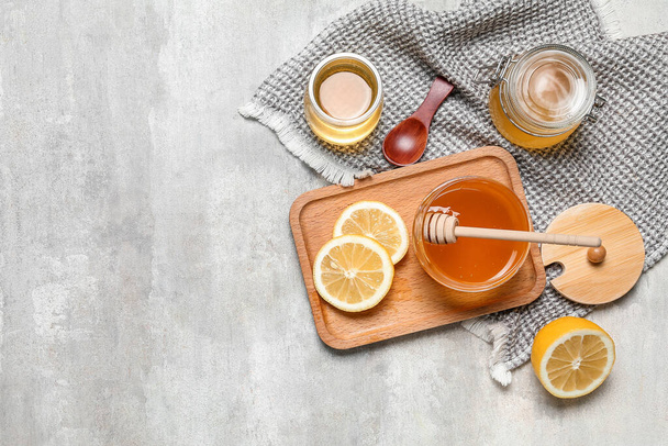 Jars of sweet honey and lemon on grey background - Fotoğraf, Görsel
