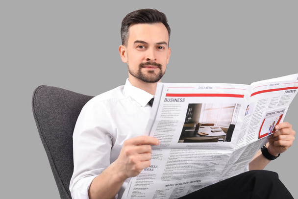 灰色の背景にアームチェアで新聞を読むハンサムなビジネスマン - 写真・画像