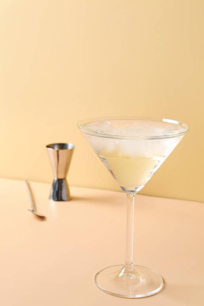 Glass of martini with ice, bar spoon and jigger on beige background - Photo, image