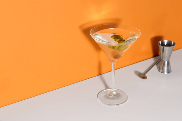 Glass of martini with olives, bar spoon and jigger on color background - Φωτογραφία, εικόνα