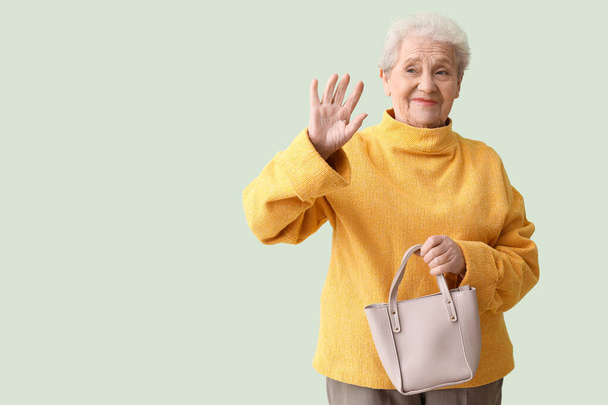Senior woman with bag waving hand on green background - Photo, Image
