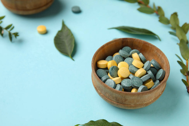 Bowl with pills and leaves on blue background, closeup - Photo, image