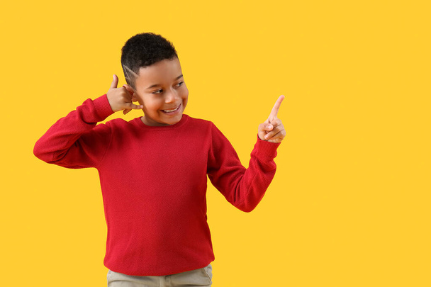 Pequeño niño afroamericano mostrando "llámame" gesto y apuntando a algo en el fondo amarillo - Foto, imagen