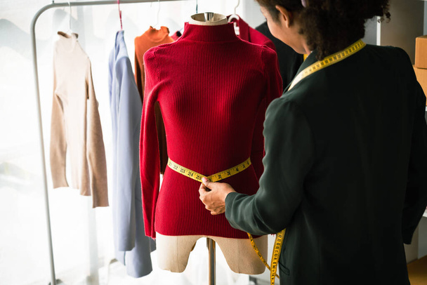 Afrikaans-Amerikaanse ontwerper vrouw controleren details en het meten van taille grootte van truien op mannequin. - Foto, afbeelding
