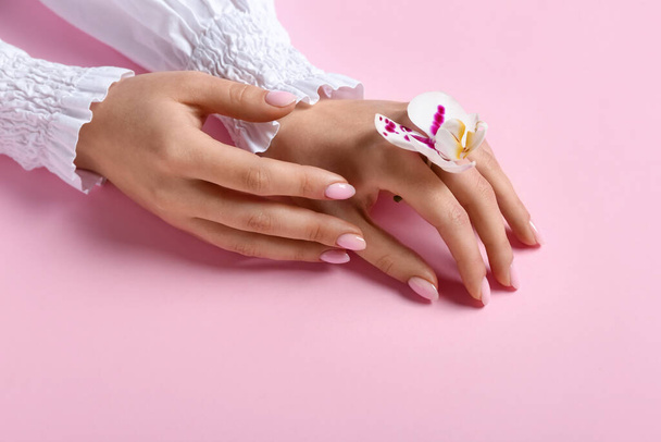 Woman with orchid flower on pink background, closeup. Hand care concept - Valokuva, kuva
