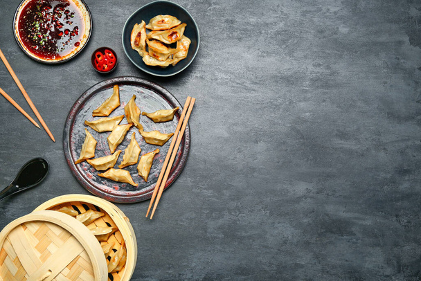 Plate with tasty Chinese jiaozi, bamboo steamer and sauce on black background - Photo, Image