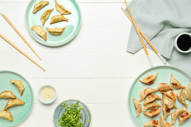 Тарелки с вкусным китайским Jiaozi, лук и соус на белом деревянном фоне - Фото, изображение