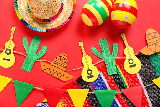 Mexikanische Maracas mit Sombrero-Hut, Papiergirlande und Fahnen auf rotem Hintergrund - Foto, Bild