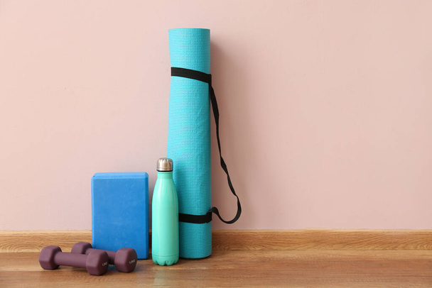 Κουδούνια με fitness mat, μπλοκ και μπουκάλι κοντά σε ροζ τοίχο - Φωτογραφία, εικόνα