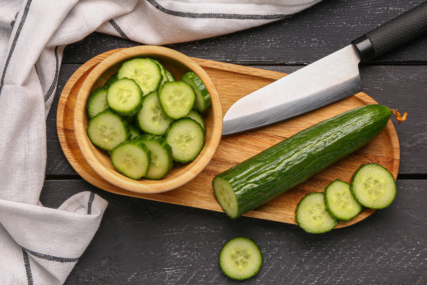 Bowl with fresh cut cucumber on dark wooden background - Photo, image