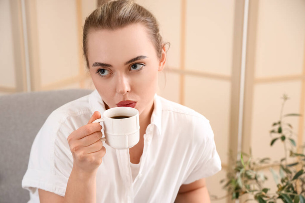 Προσεκτική νεαρή γυναίκα με φλιτζάνι καφέ κάθεται στον καναπέ στο σπίτι, closeup - Φωτογραφία, εικόνα