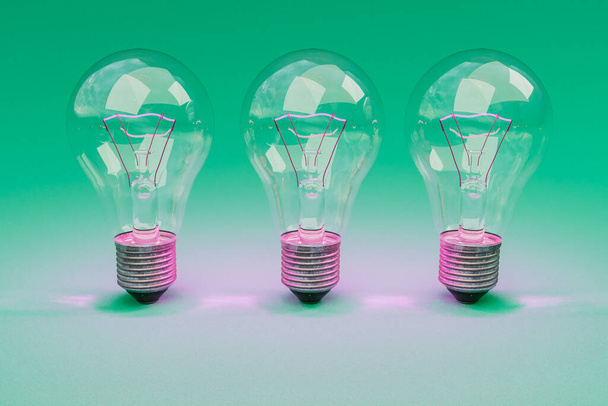 три лампочки в стиле ретро с светящимися нитями, стоящими в ряд на бесконечном красочном фоне; концепция дизайна креативности; 3D иллюстрация - Фото, изображение